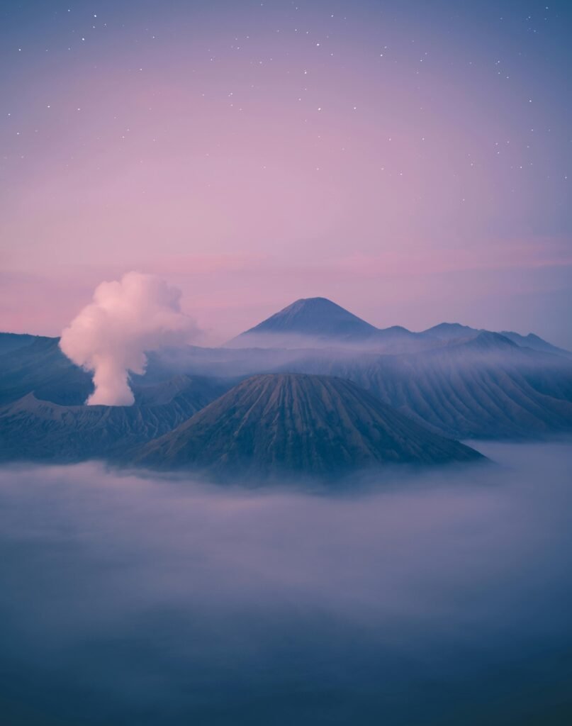 A picturesque view of Mount Bromo surrounded by mist and a pastel sky at dawn, capturing nature's serene beauty.